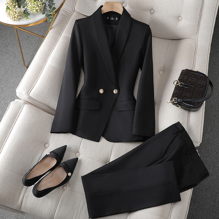 Ein schwarzer Blazer und eine passende Hose, arrangiert auf einer weichen Unterlage, begleitet von spitzen schwarzen Pumps und einer kleinen Handtasche.